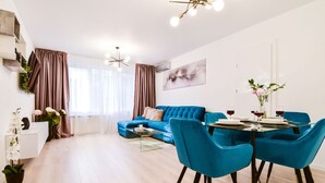 A modern living room with a blue sofa, a dining table with blue chairs, and a glass coffee table.