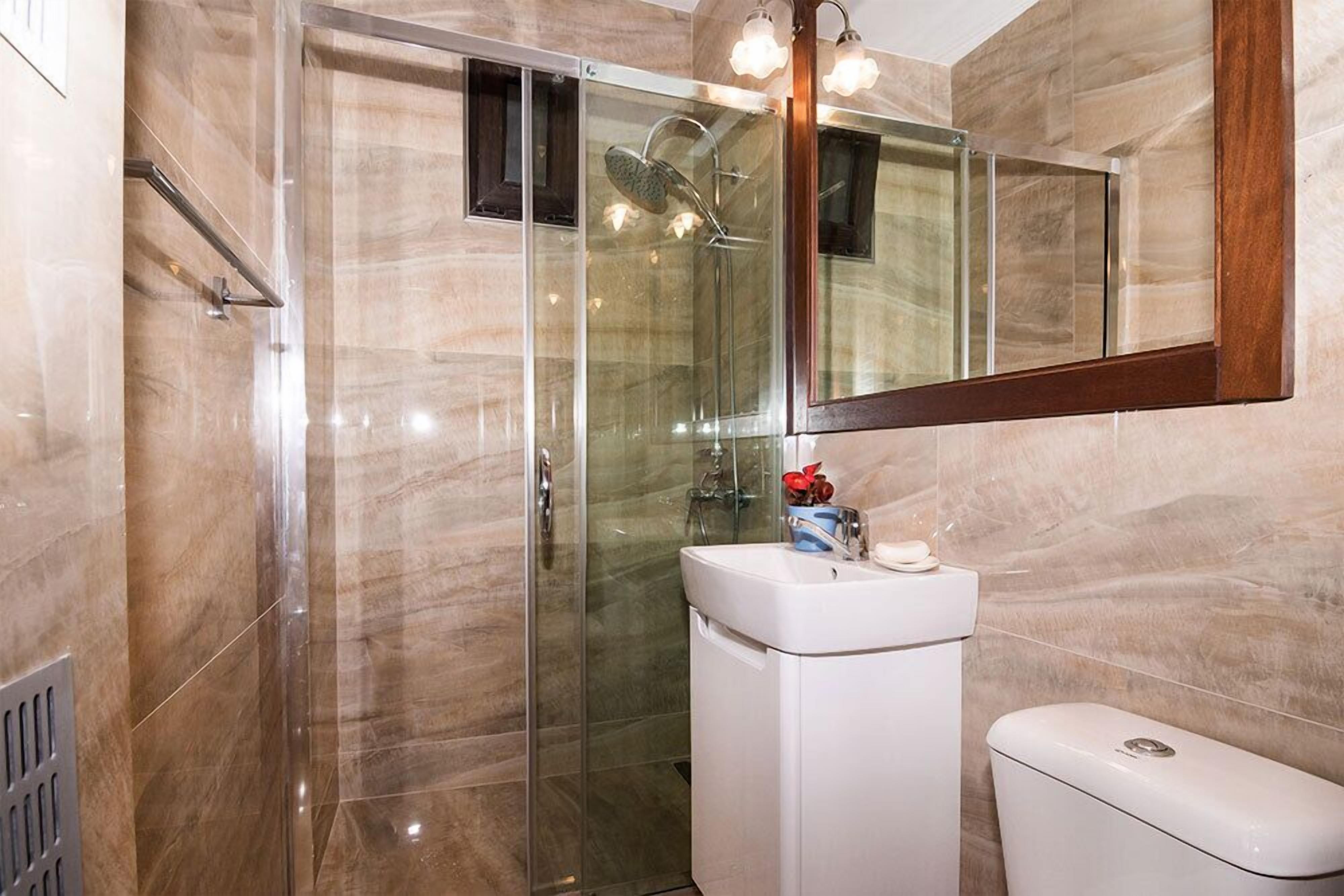 Un baño moderno con ducha envuelta en vidrio, un lavabo blanco y un espejo grande.