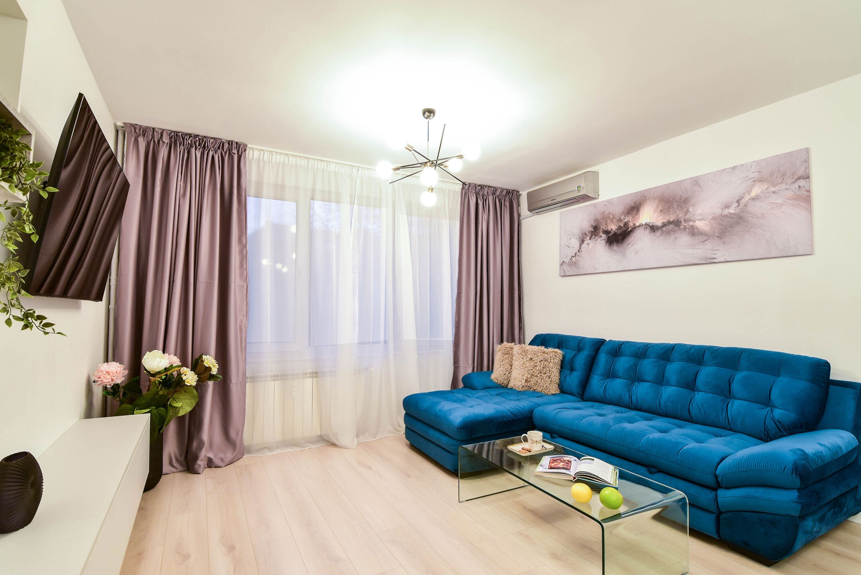 Een moderne woonkamer met een blauwe bank, een glazen salontafel en een witte bijzettafel.