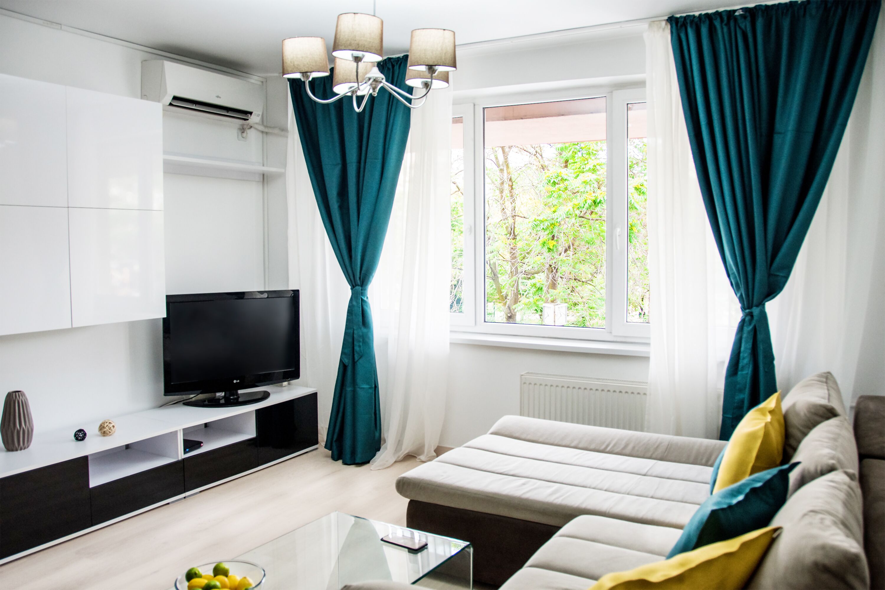 Ein modernes Wohnzimmer mit Flachbildfernseher, einer Couch, einem Couchtisch und lindgrünen Vorhängen.