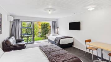 A hotel room with a large bed, a sofa, a dining table, and a TV.