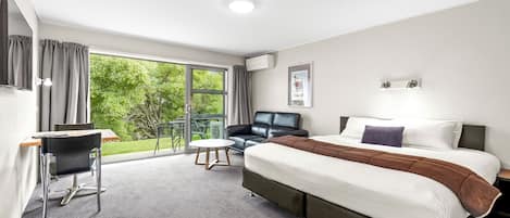 A hotel room with a large bed, a desk, a chair, and a view of the outdoors.