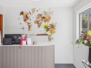 Een receptiebalie met een wereldkaartmuur, een bureaulamp, een bloevas en een raam met uitzicht op groen.