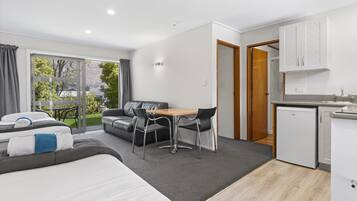 Una habitación de hotel moderna con una cama, un área de comedor con mesa y sillas, una kitchenette y un puerta corrediza de vidrio que da a un balcón.
