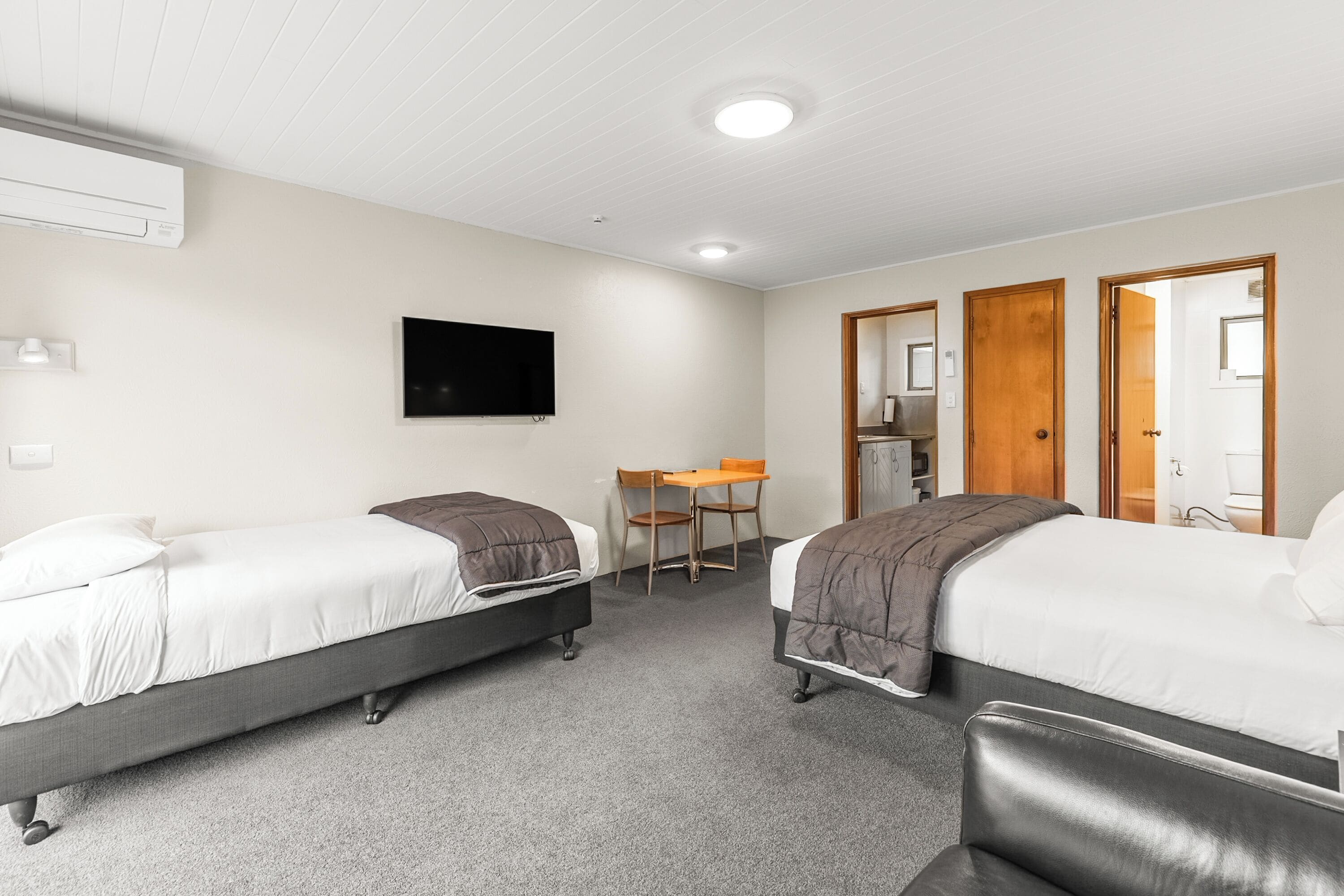 Una habitación de hotel con dos camas individuales, un escritorio, una silla y un televisor en la pared.