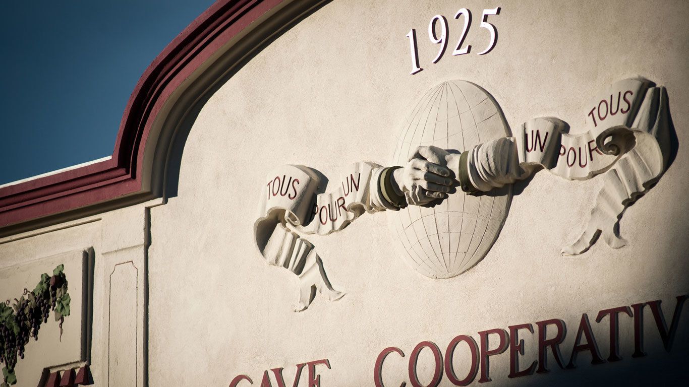 Fachada de edificio con el año 1925 y las palabras 'TOUS POUR UN' y 'COOPERATIV' a la vista.