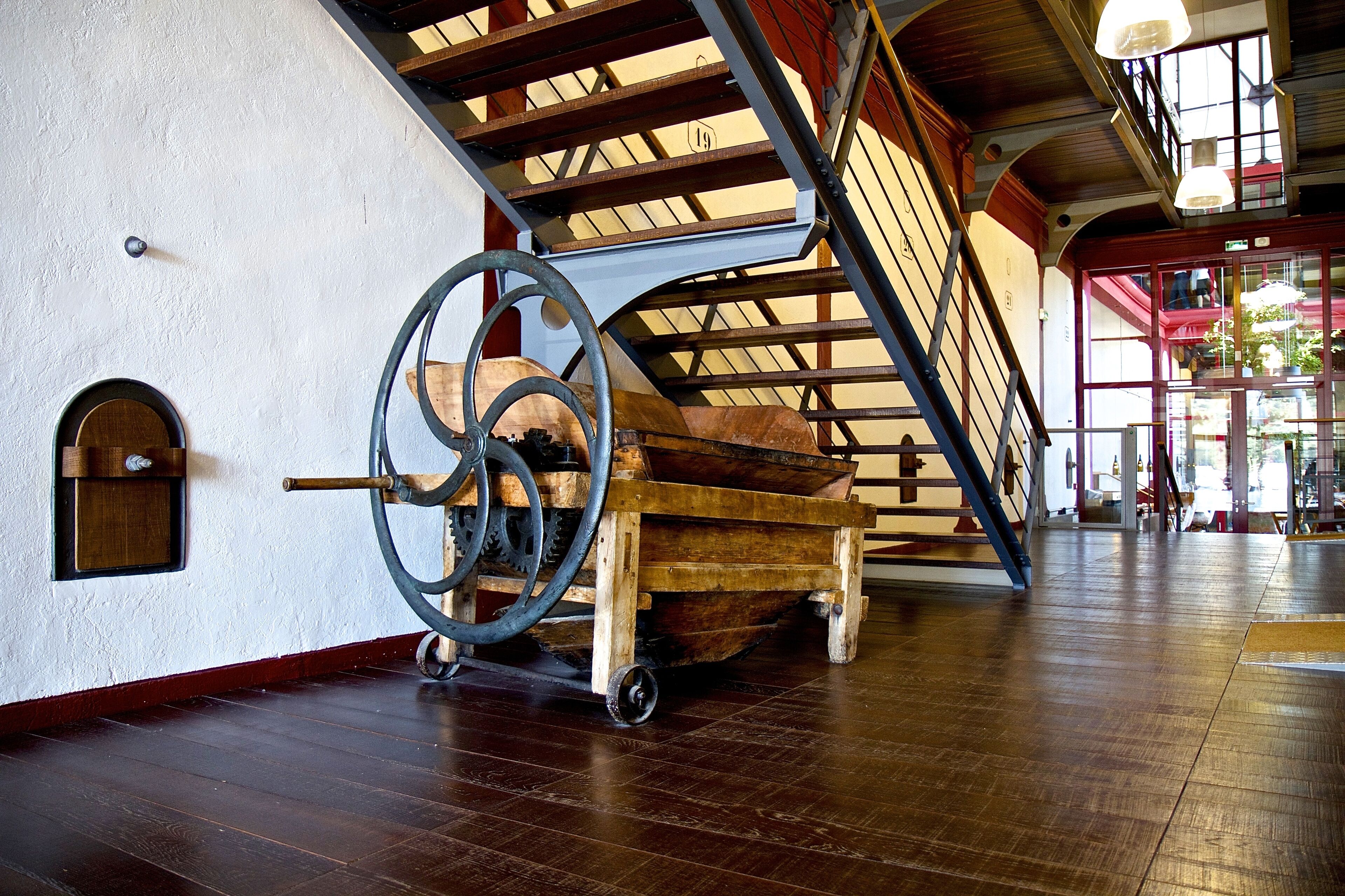 Un carretto di legno dotato di grandi ruote e un sistema di carrucole in una stanza ampia con pavimento in legno e soffitto alto.