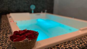 A spa tub with a blue light, a basket of red roses, and a stone-patterned floor.