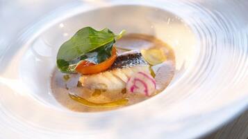 A white bowl with a fish dish, garnished with a leaf and radish slices.