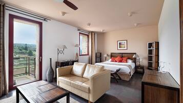 Una habitación amplia con cama, sofá, mesa y balcón con vistas al campo.