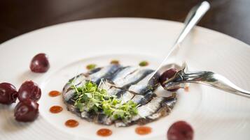 Un plato blanco con pescado en rodajas, adornado con vegetales verdes y rodeado de tomates cherry.