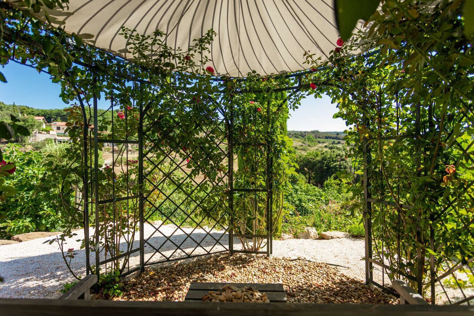 Un kiosque doté d’une structure en treillis, entouré de gravier et de plantes.