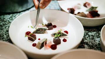 Una persona usando pinzas para servir un plato con diversos alimentos sobre una fuente blanca.