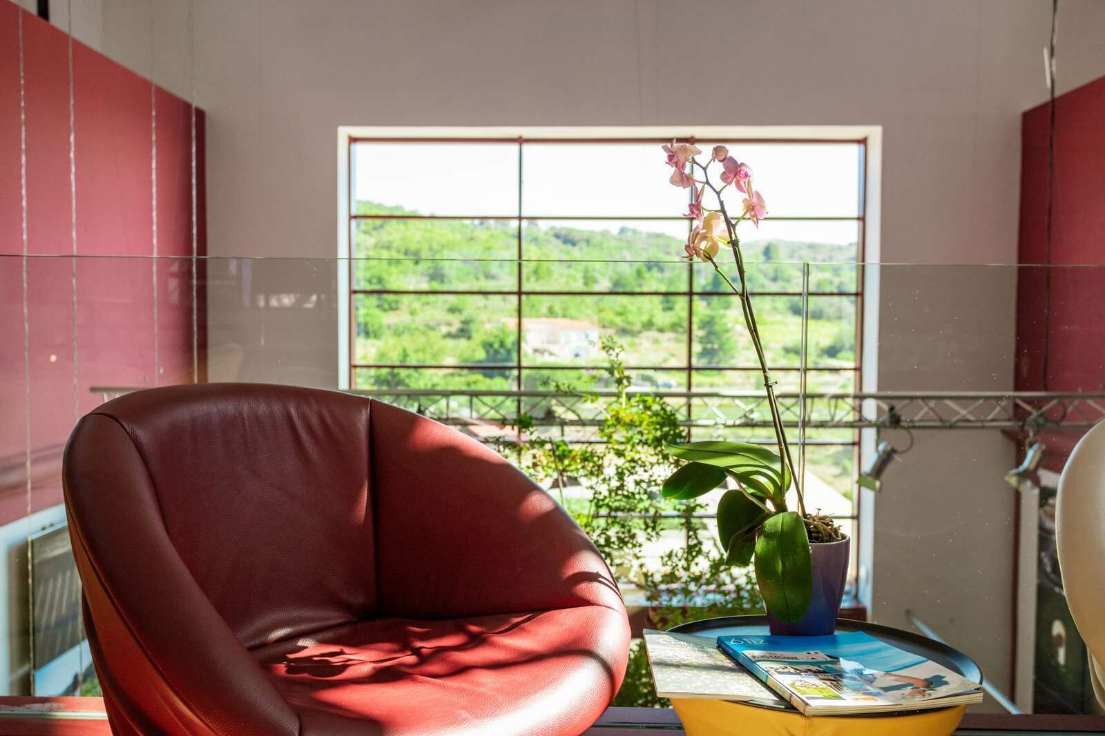 A room with a leather chair, a table with a book, and a window with a view of greenery.