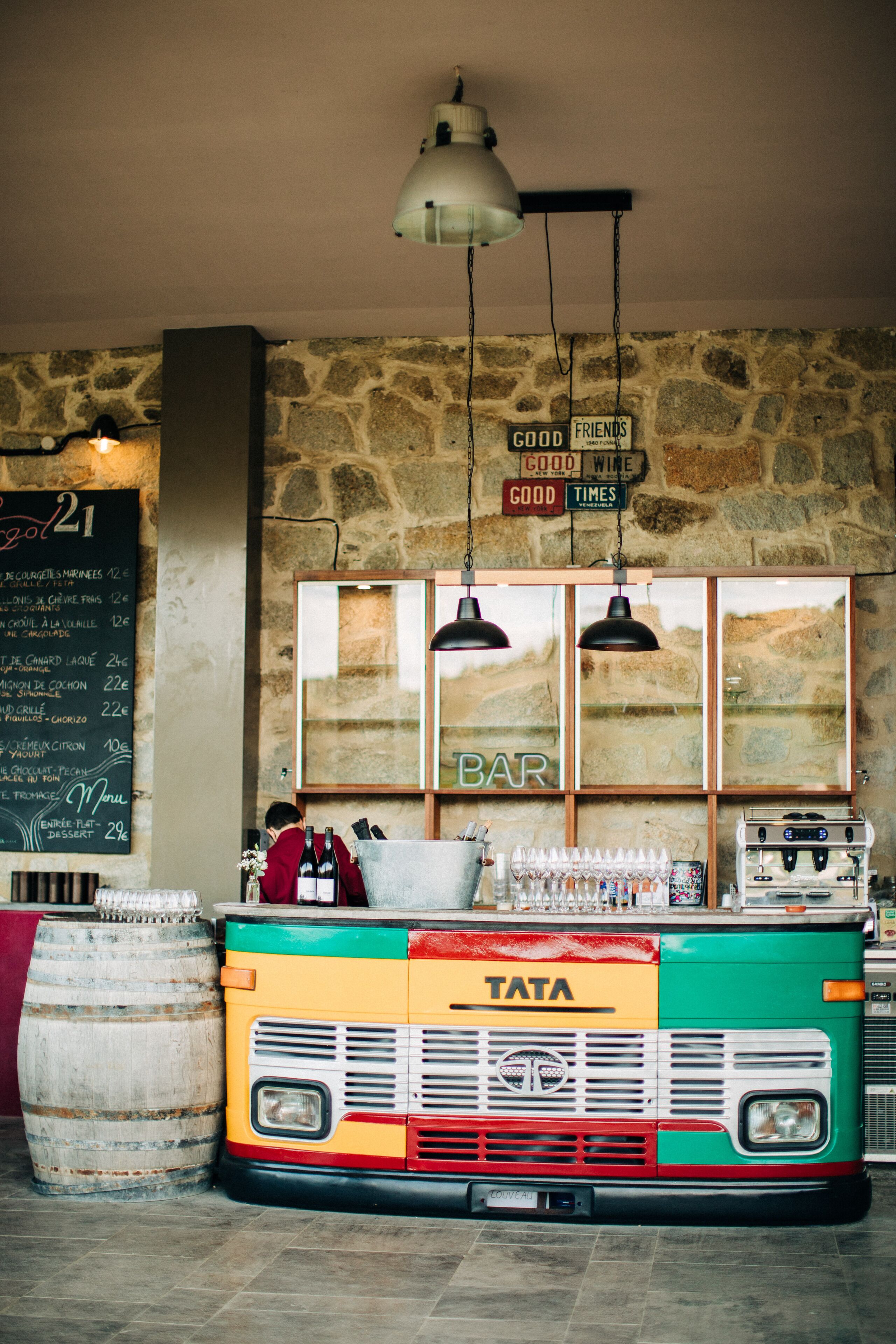 A vintage TATA bus converted into a bar with a stone wall backdrop and hanging lights.