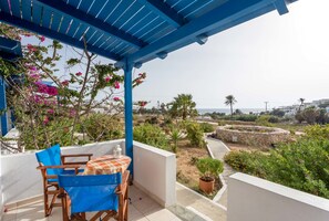A balcony with a blue pergola, a table with chairs, and a view of the landscape.
