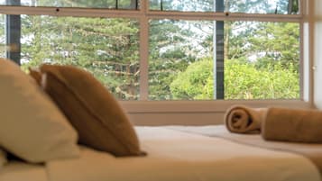 A bed with pillows and a rolled towel, a window with a view of trees.