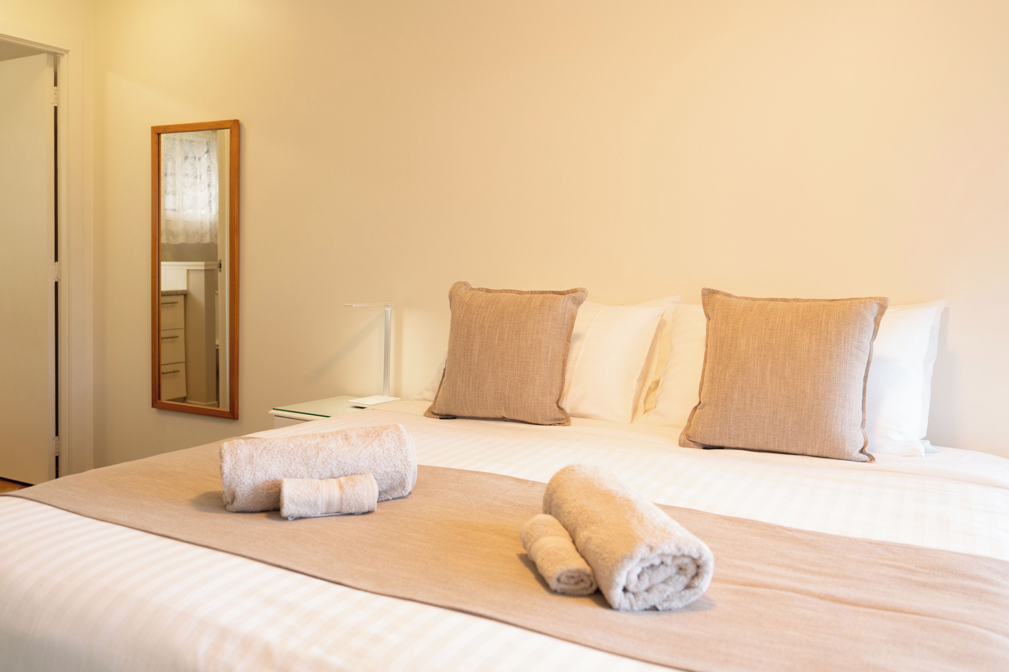 A neatly made bed with two pillows and two rolled towels on a white bedspread.