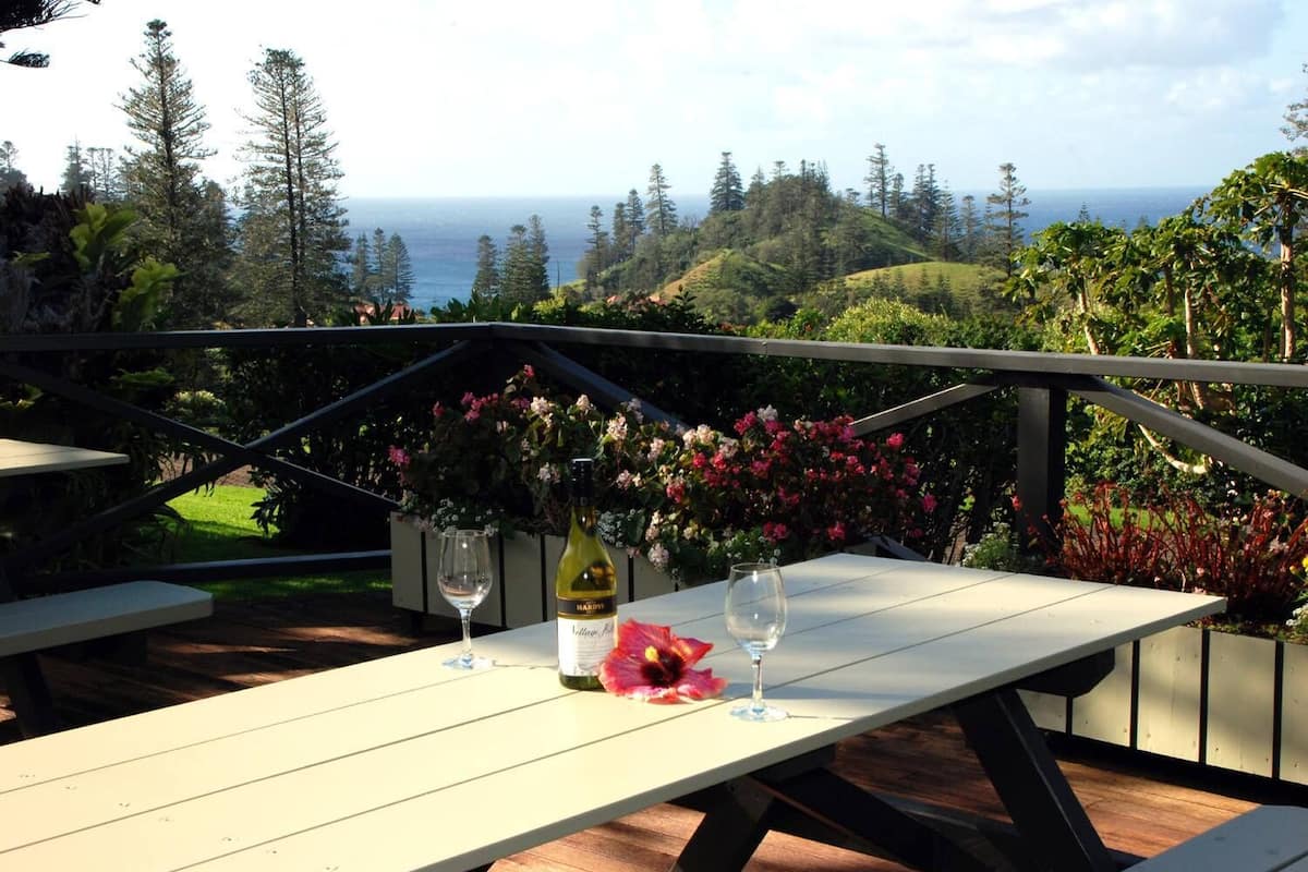 A table with a bottle of wine and two glasses, set against a backdrop of a scenic view with hills and the ocean.