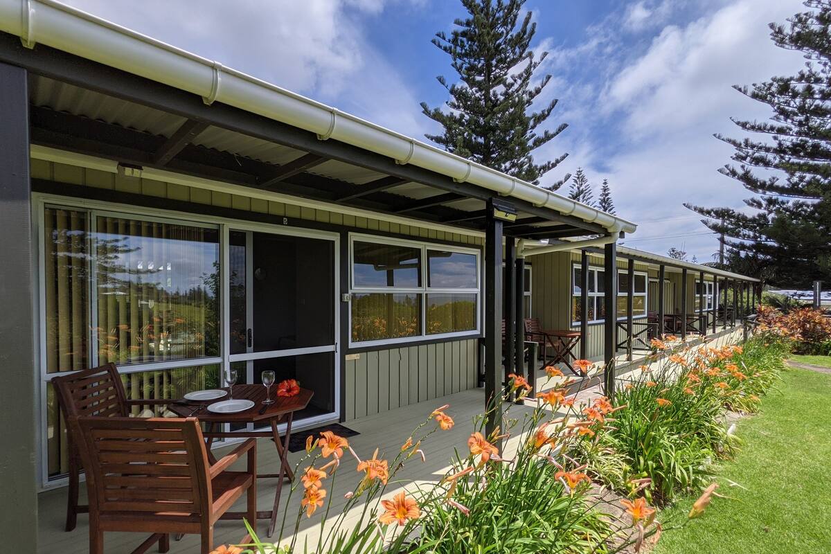 A modern building with large windows, outdoor seating, and a garden with flowers.