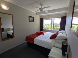Une chambre d’hôtel avec un lit, une table de chevet, un miroir, un ventilateur de plafond et une fenêtre avec des rideaux.