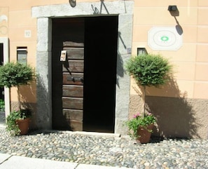 A building entrance with a stone archway, a doorbell, and two potted plants on either side. - Hotel Casa Arizzoli (Cannobio)
