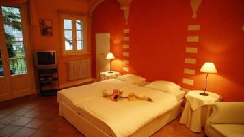 Habitación de hotel con una cama grande, dos lámparas de noche, un televisor y una ventana con vista a palmeras.