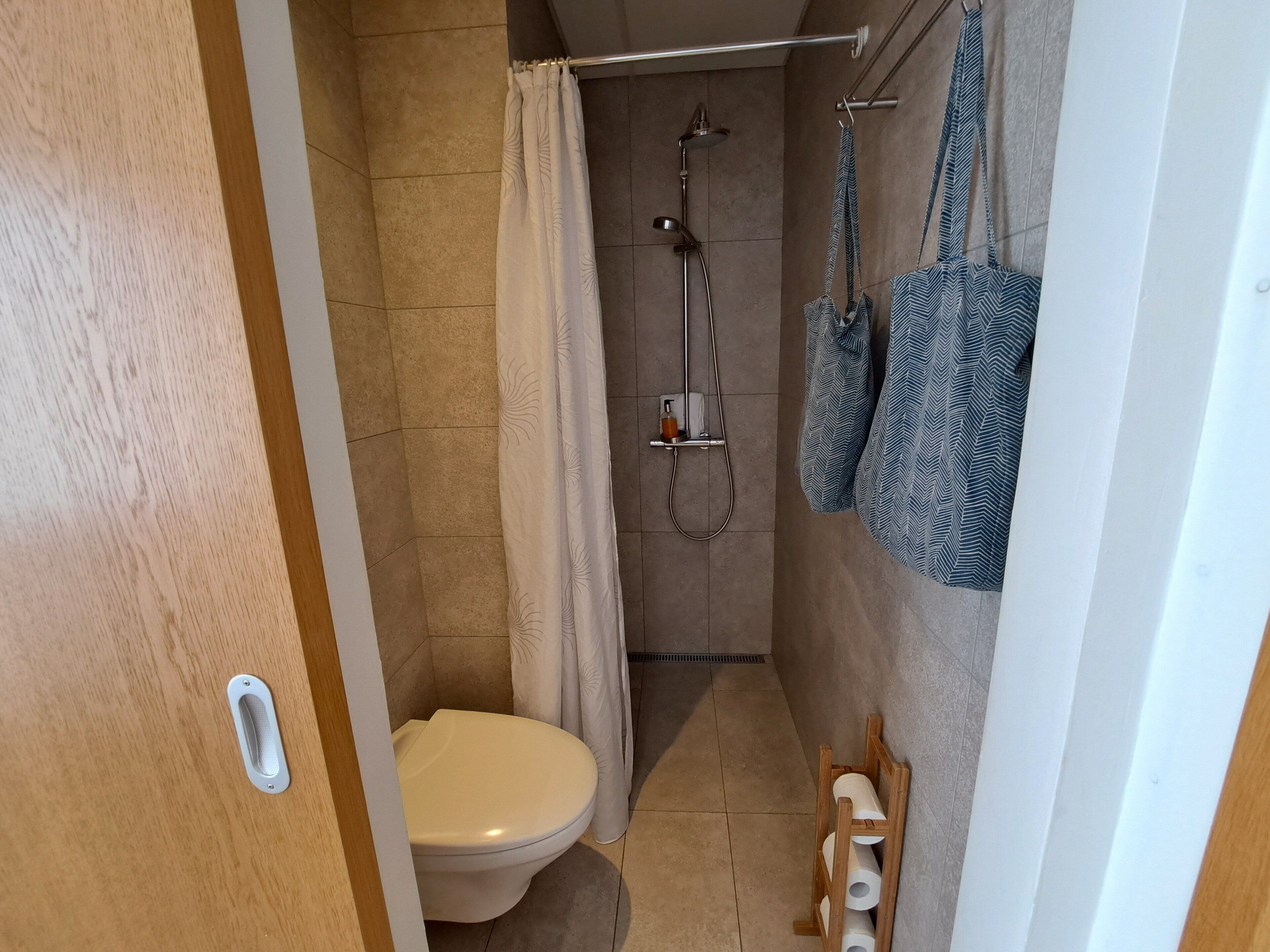 A small bathroom with a toilet, shower, and towel rack.