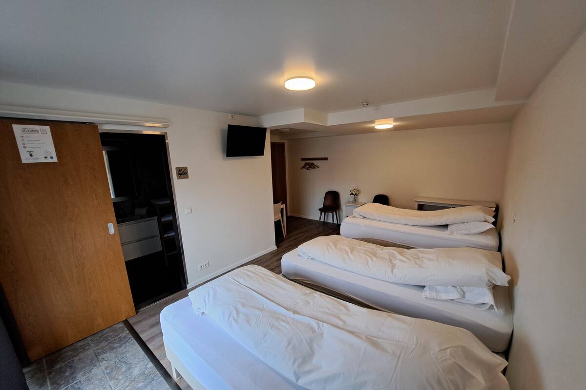 Habitación de hotel con tres camas, un televisor montado en la pared y una puerta de madera.