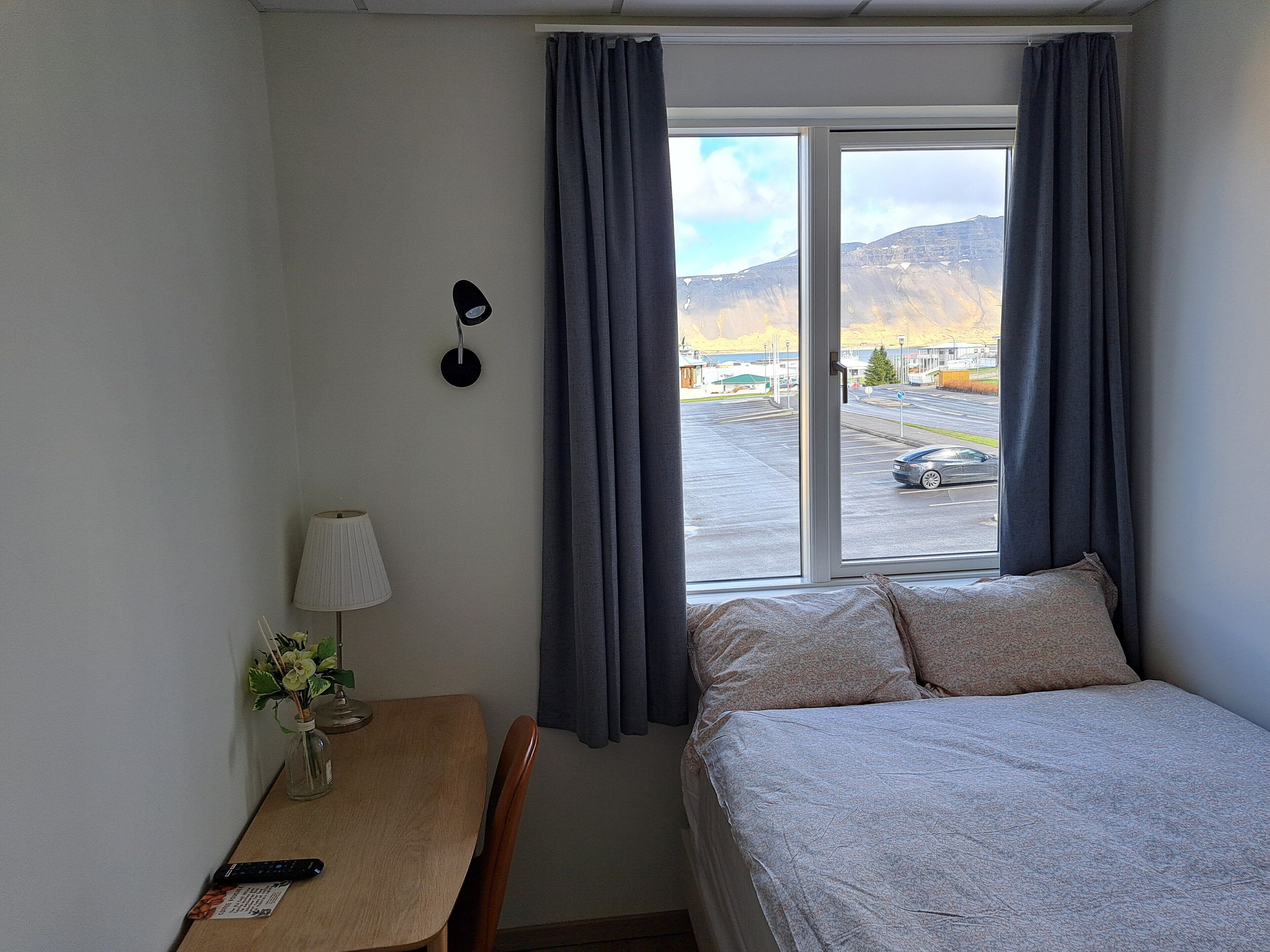 Ein Hotelzimmer mit Bett, Schreibtisch mit Lampe und einem Fenster mit Vorhängen.
