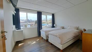 A hotel room with two beds, a small desk, a window with curtains, and a view of the mountains.