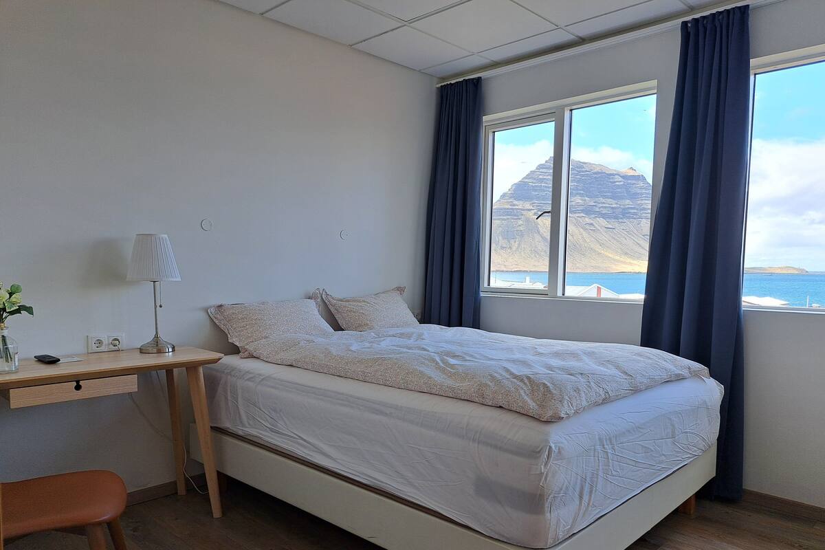 Un dormitorio con cama, escritorio, silla y ventana con cortinas.