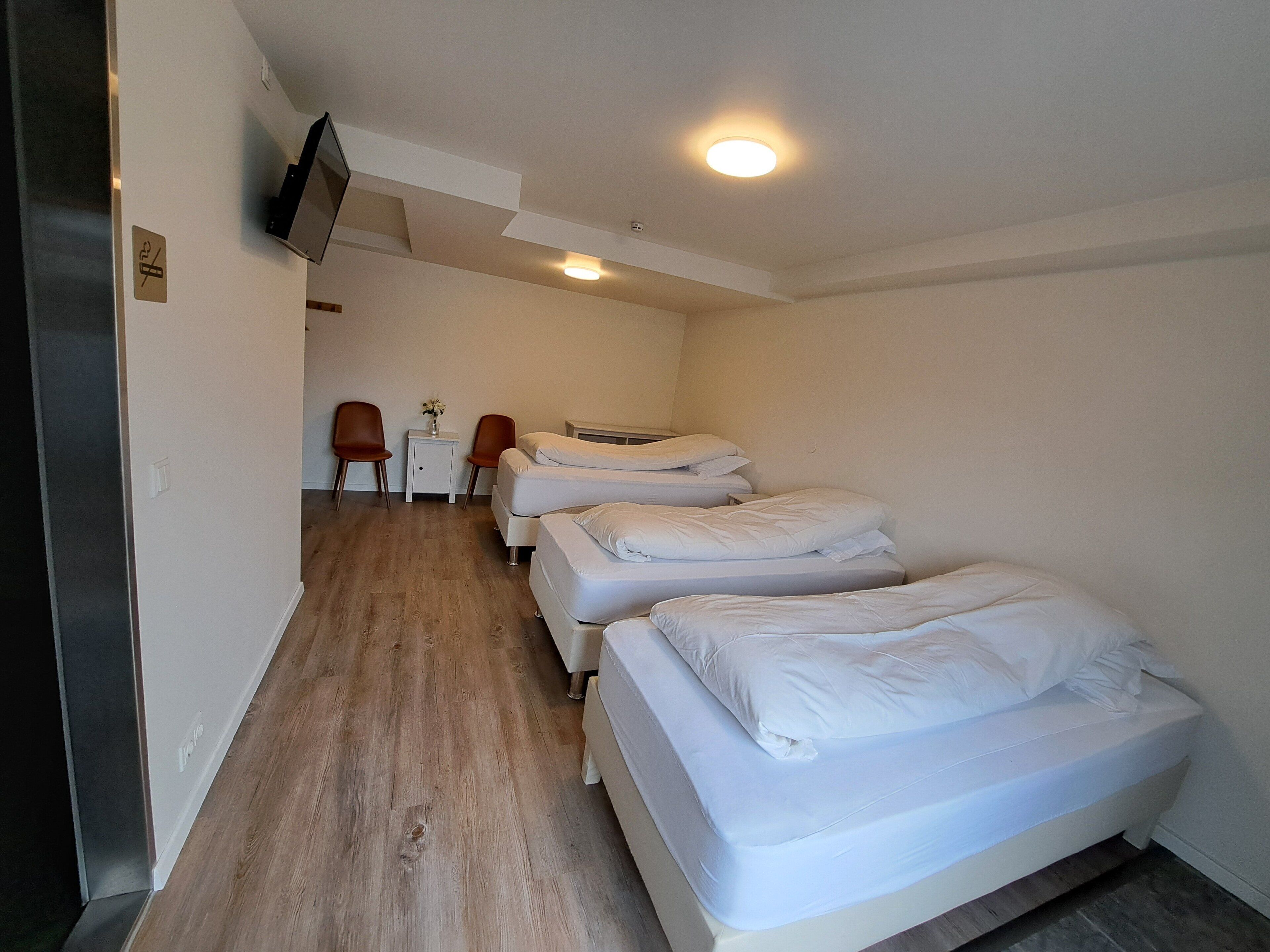 A hotel room with three beds, a small table with a vase, and two chairs.
