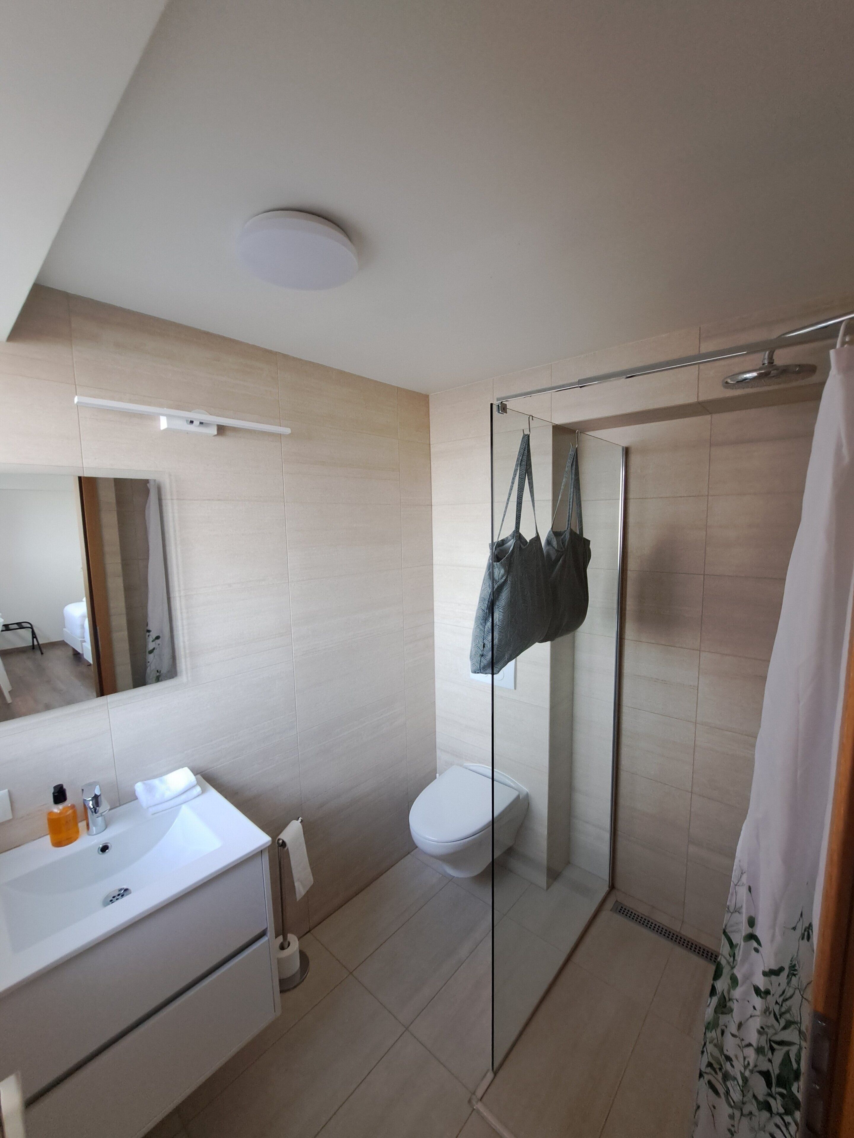 Un baño moderno con cabina de ducha de vidrio, un lavabo blanco con espejo y un inodoro.