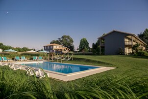 A swimming pool with lounge chairs and a hammock, surrounded by well-maintained lawns and trees.