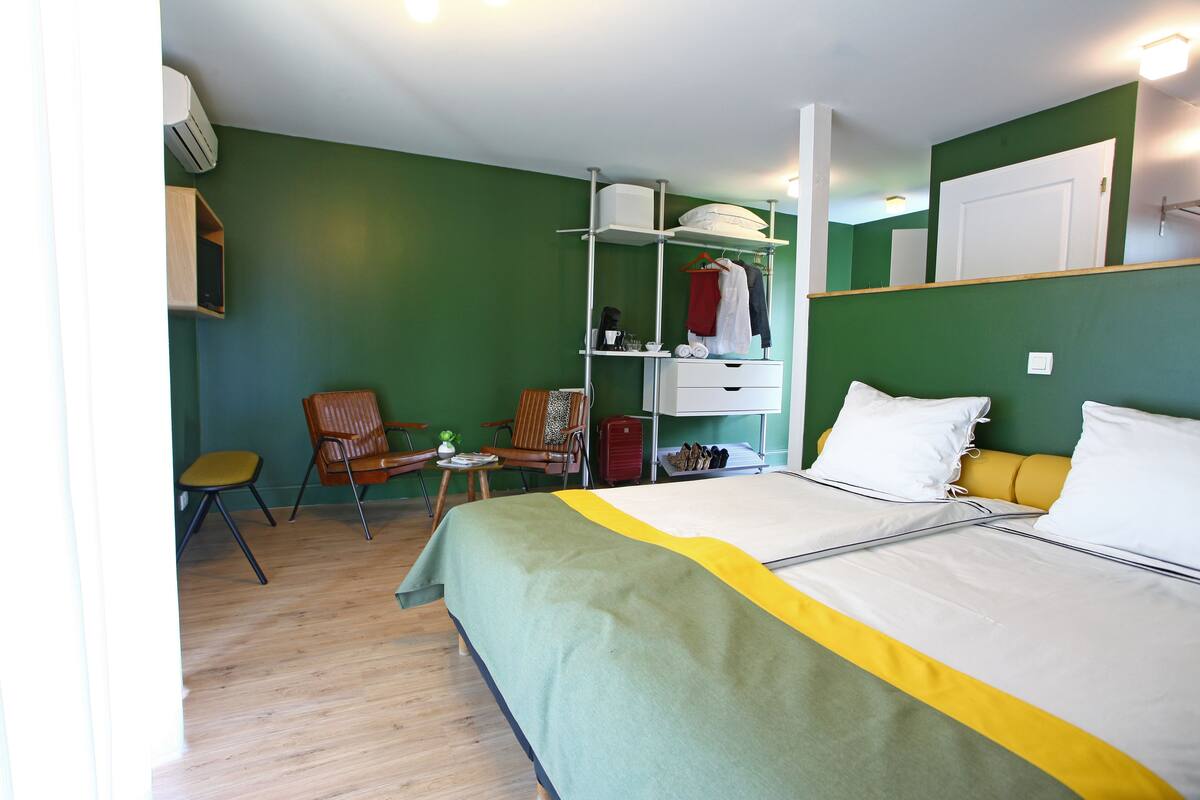 Une chambre d’hôtel comprenant un lit, une chaise, une petite table, une étagère avec des vêtements et une armoire.