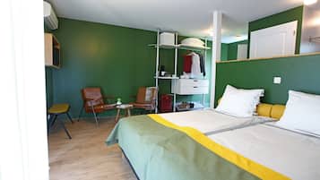 Habitación de hotel con cama, una silla, una mesita, un estante con ropa y un armario.