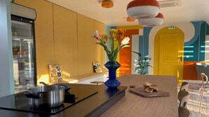 A modern kitchen with a central island, a refrigerator, and a yellow door. - La Petite Couronne, Ecolodge & Lofts (Saint-Cricq-Chalosse)
