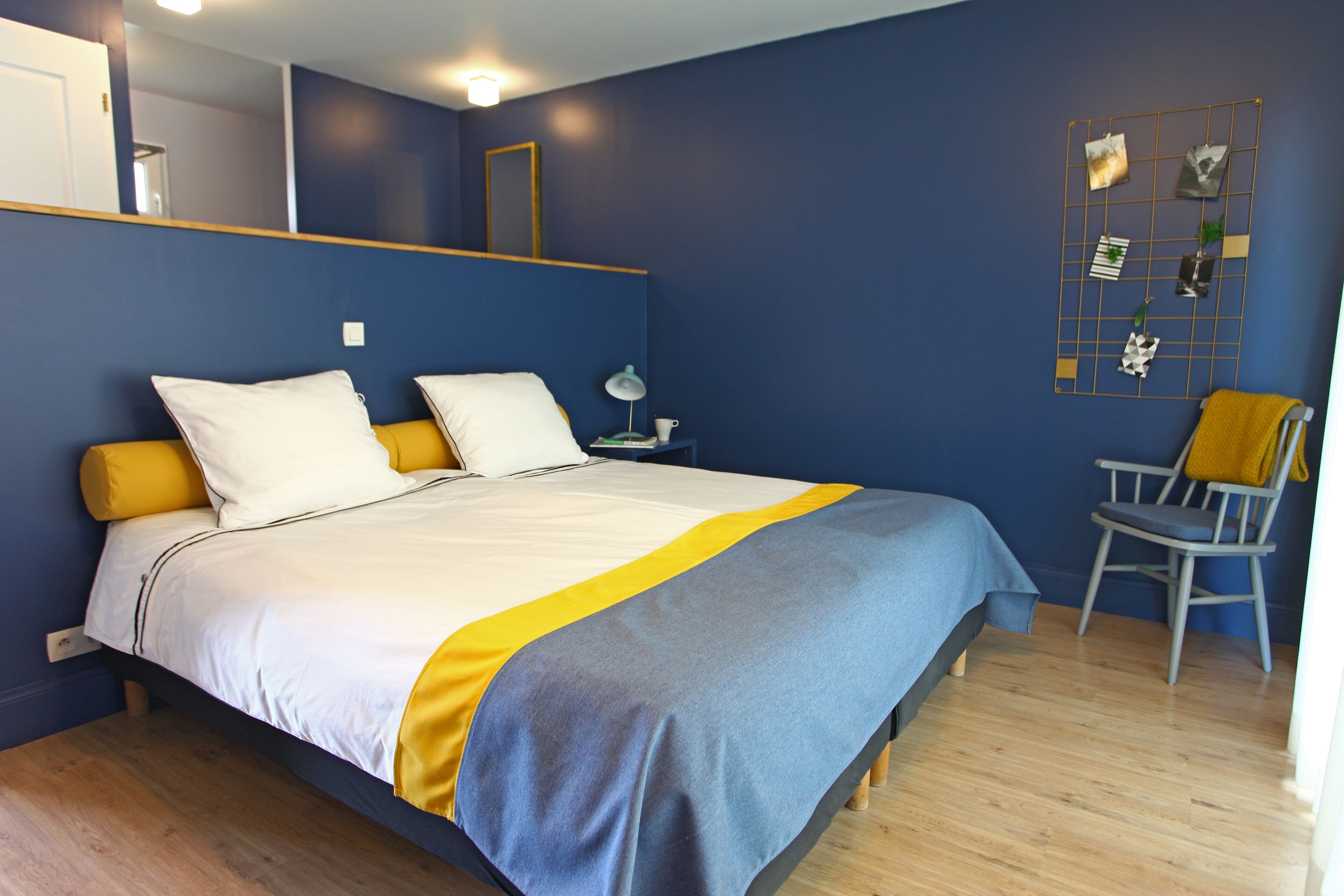 A bedroom with a bed, bedside table, chair, and a wall-mounted photo display.