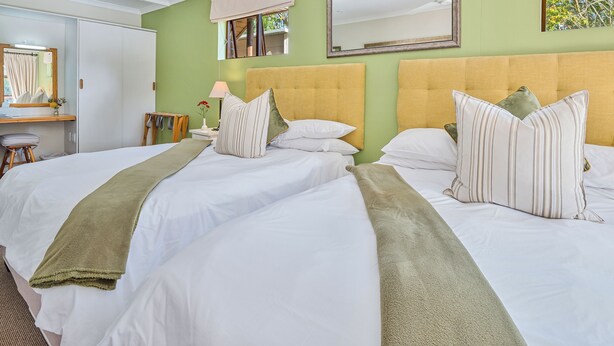 Une chambre d’hôtel avec deux lits, un bureau avec une chaise, un miroir et une fenêtre donnant sur des arbres.