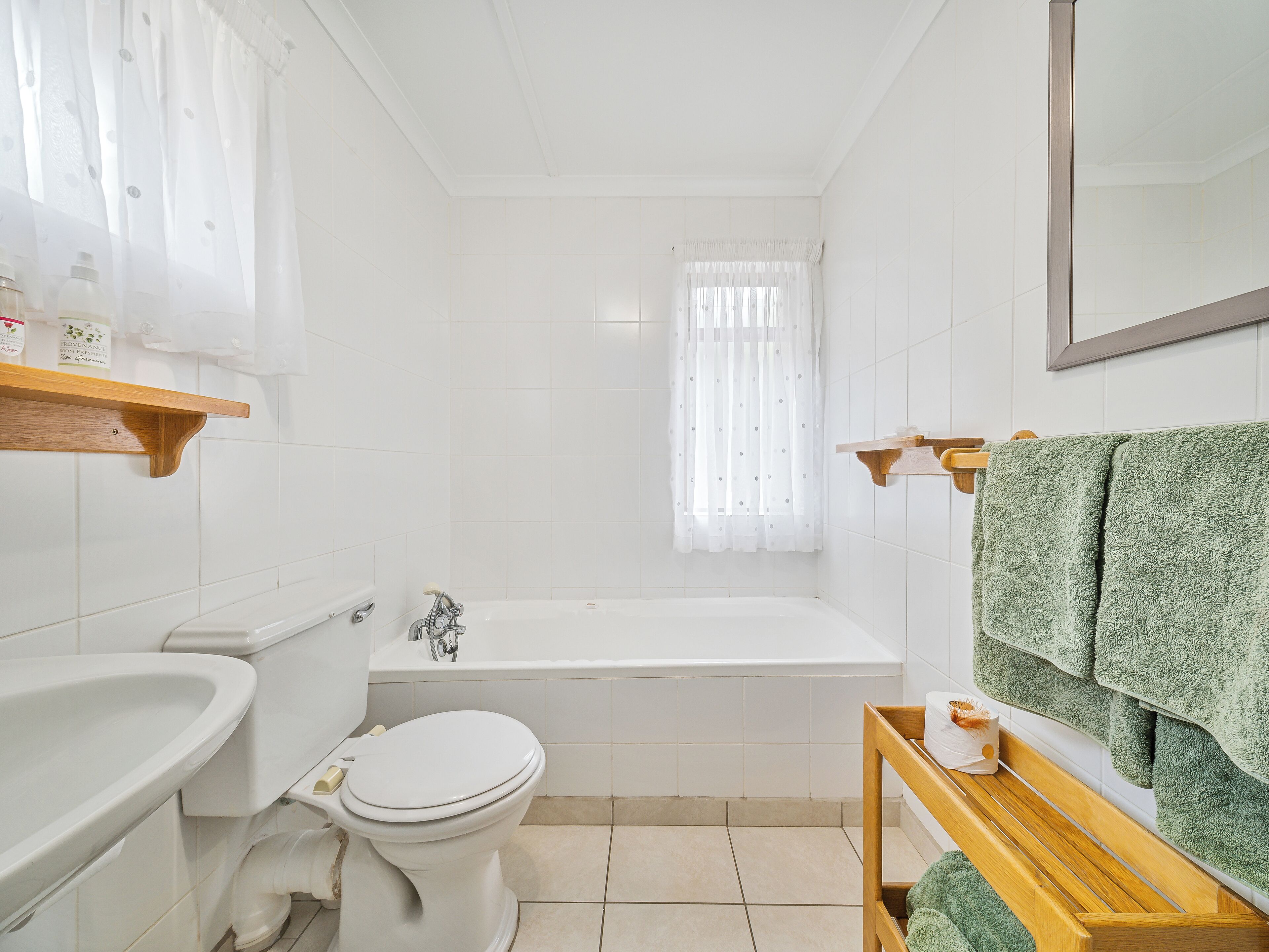 A bathroom with a toilet, sink, bathtub, and wooden shelves.