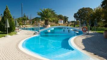 Relax by the curved pool surrounded by lush greenery and a brick-patterned walkway.