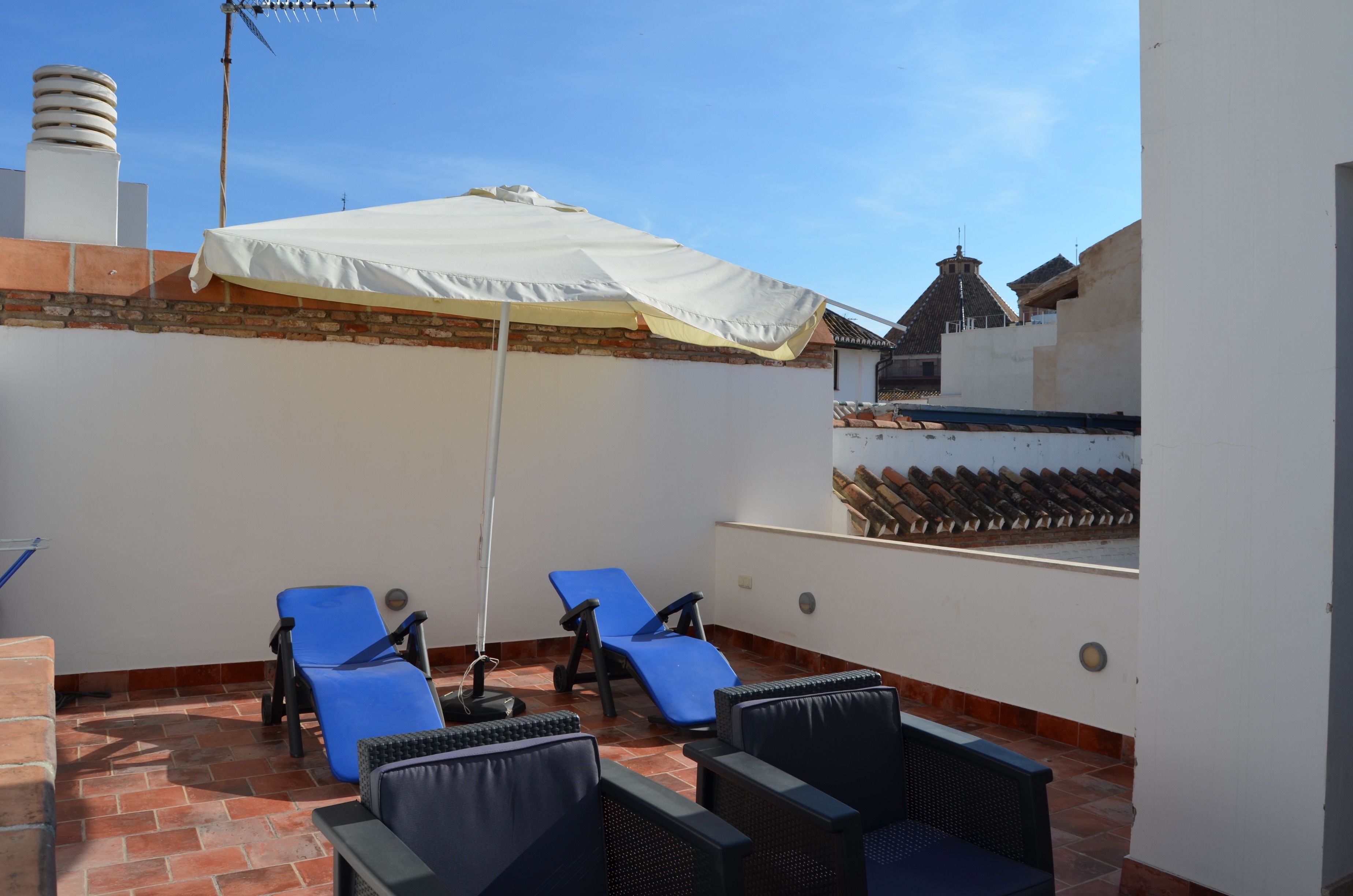 Eine Dachterrasse mit zwei blauen Liegestühlen, einem weißen Sonnenschirm und einer Ziegelwand.