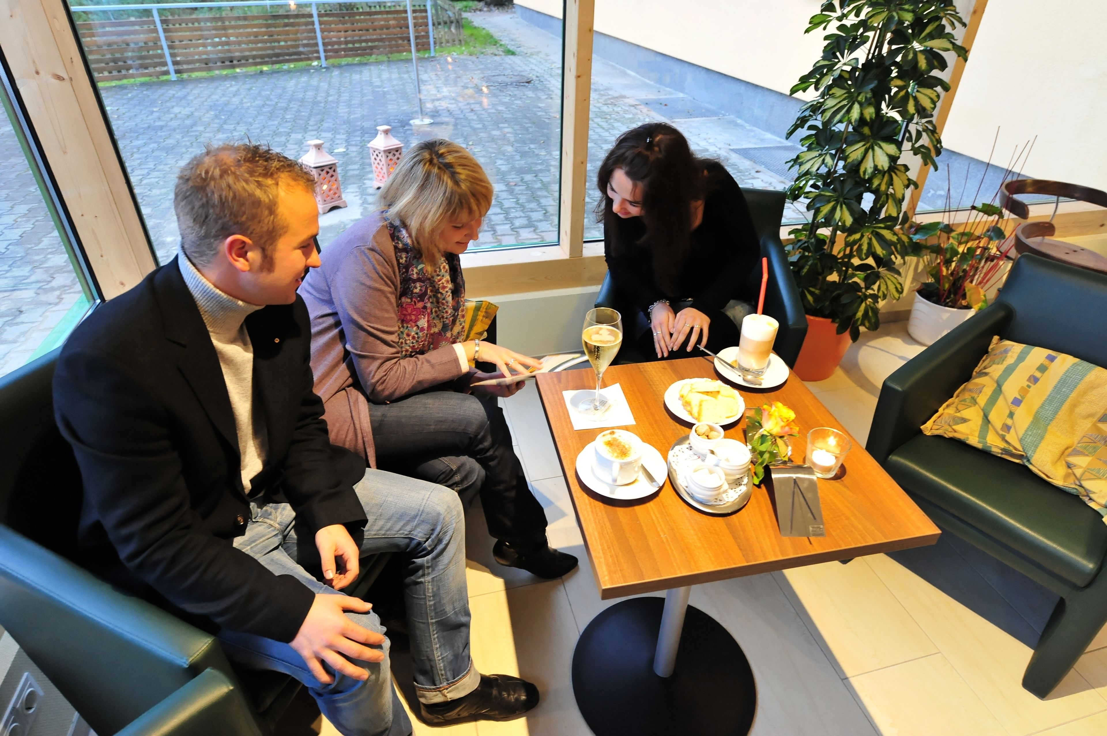 Un grupo de personas sentadas a una mesa con platos de comida, una bebida y una vela. Hay una planta y un sofá al fondo.
