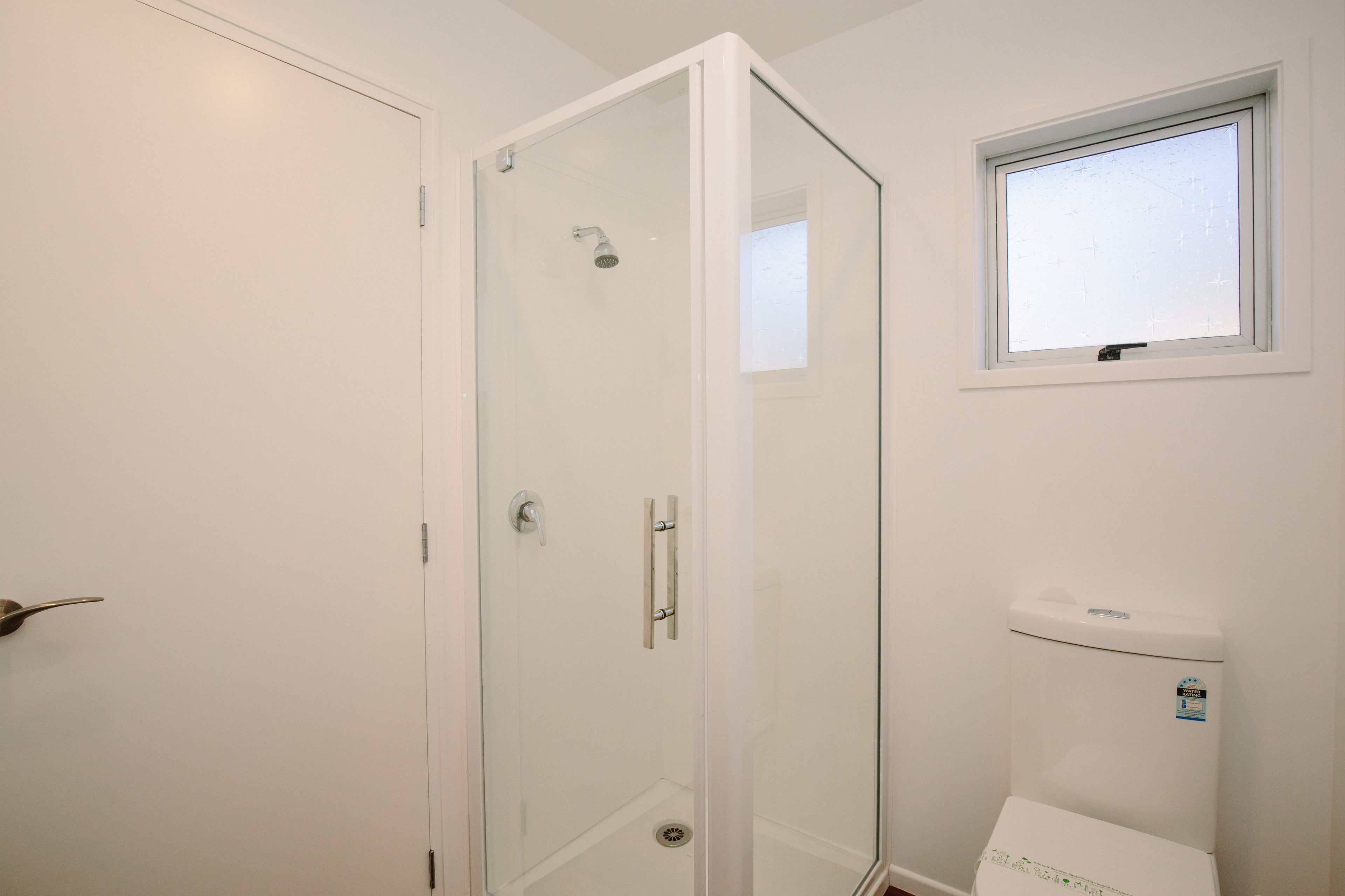 Ein Badezimmer mit Duschkabine aus Glas, Toilette und Fenster.