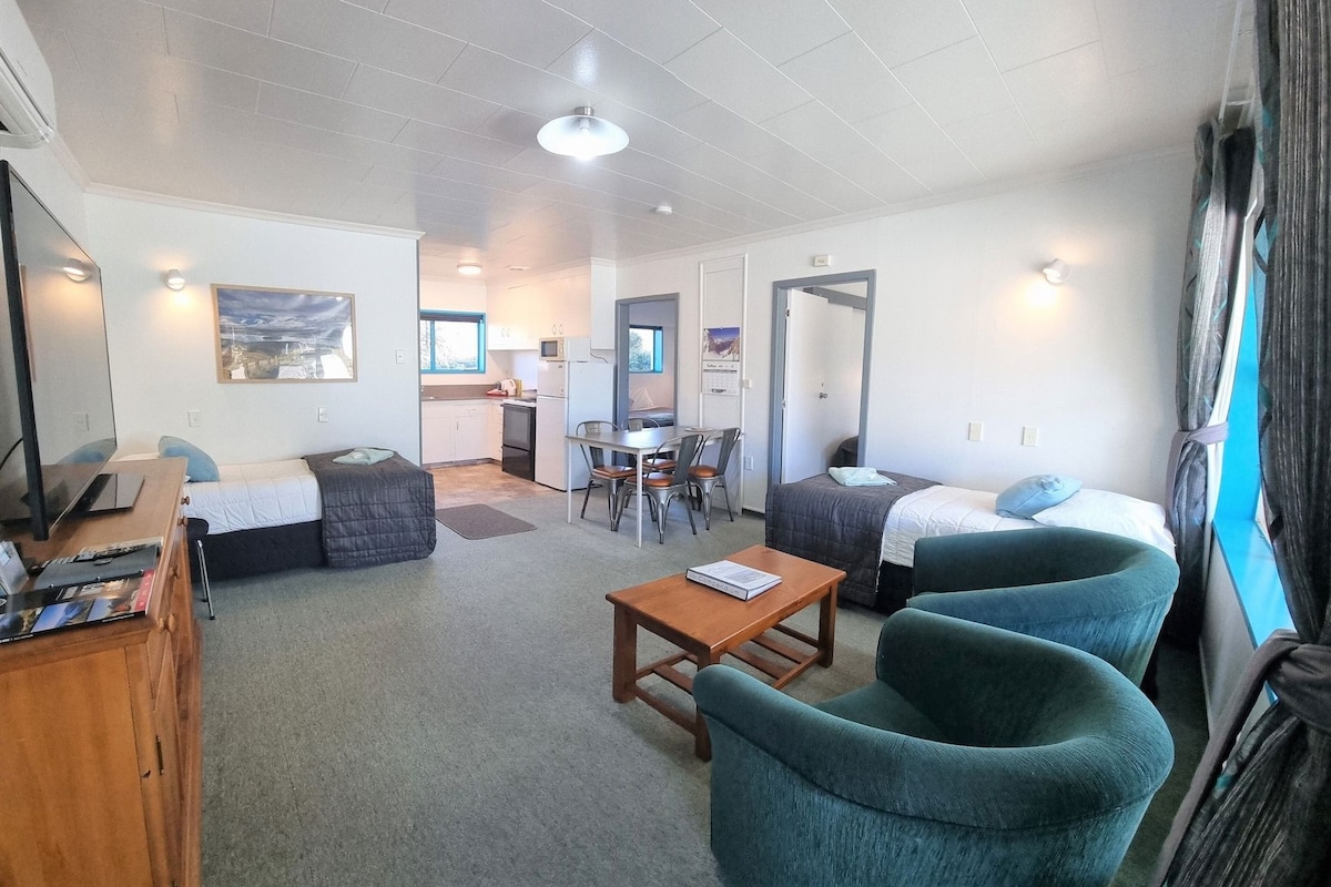 A compact hotel room with a kitchenette, a single bed, a desk, and a TV.