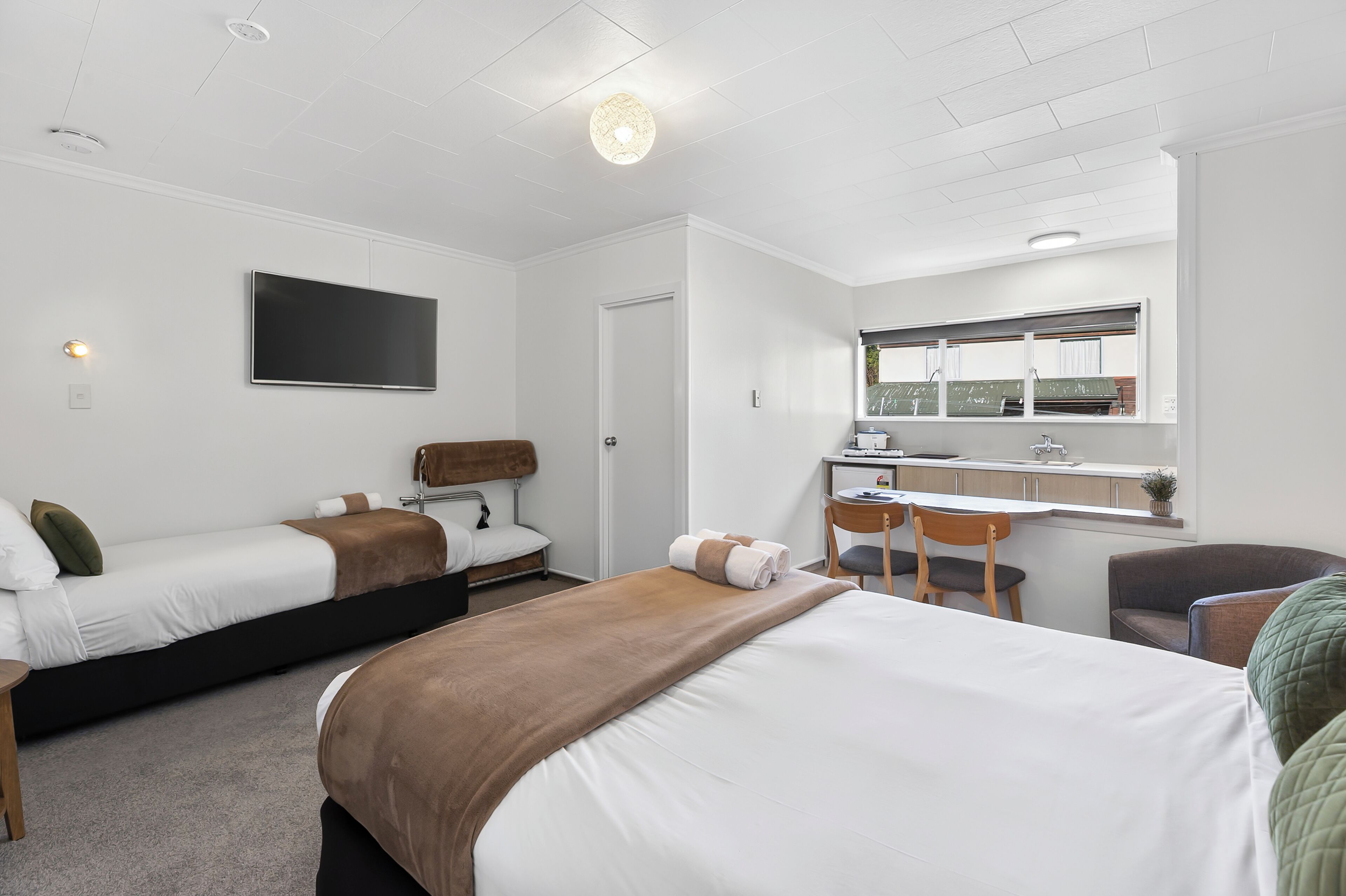 A hotel room with two beds, a desk, a chair, a small table, and a window with a view.