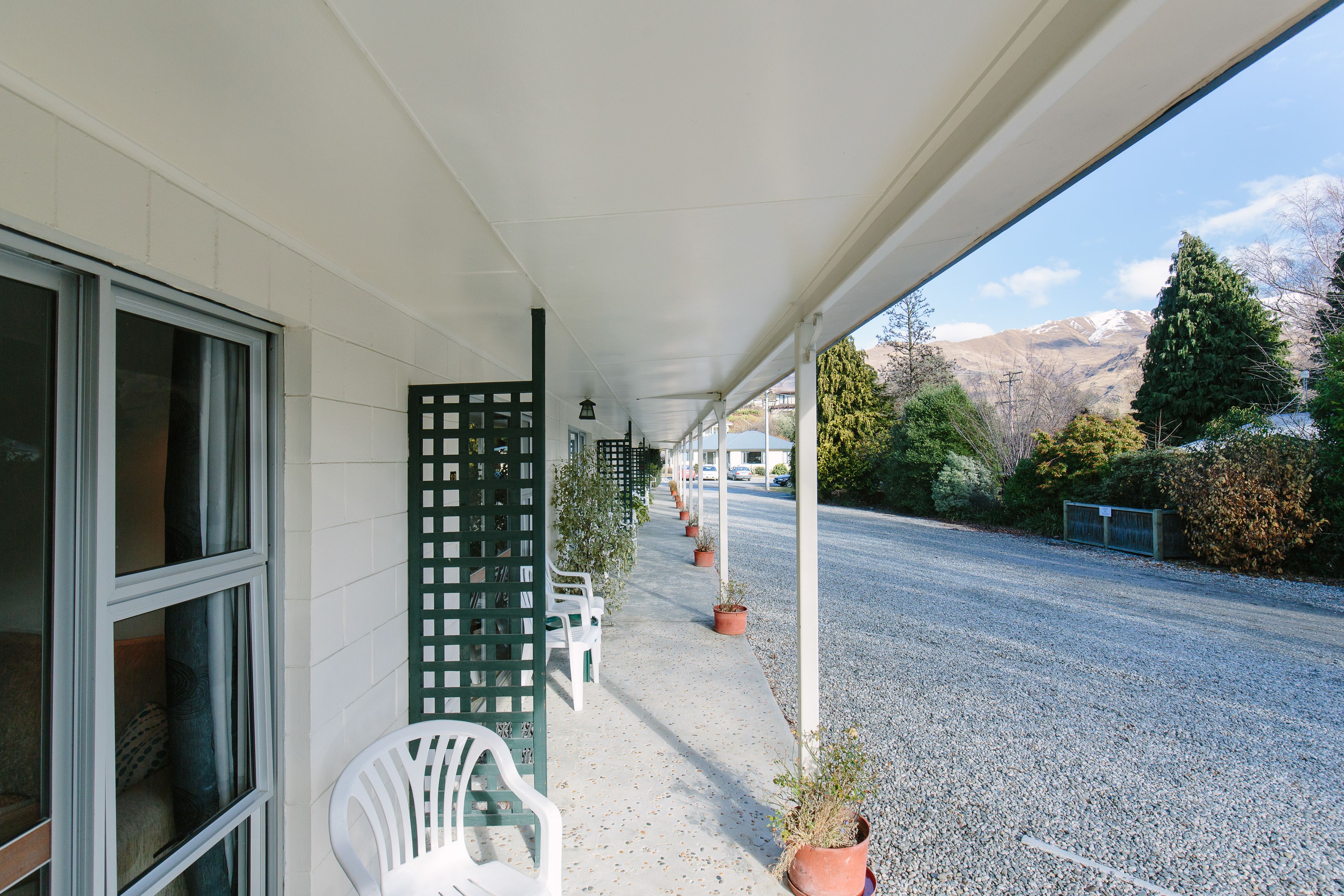 Un espace extérieur abrité, avec une rangée de chaises blanches, des plantes en pot et une vue sur une route et des montagnes.