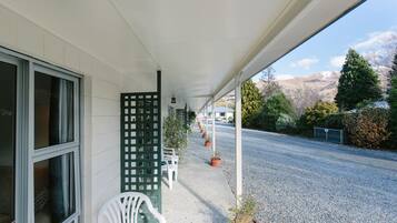 Un espace extérieur abrité, avec une rangée de chaises blanches, des plantes en pot et une vue sur une route et des montagnes.