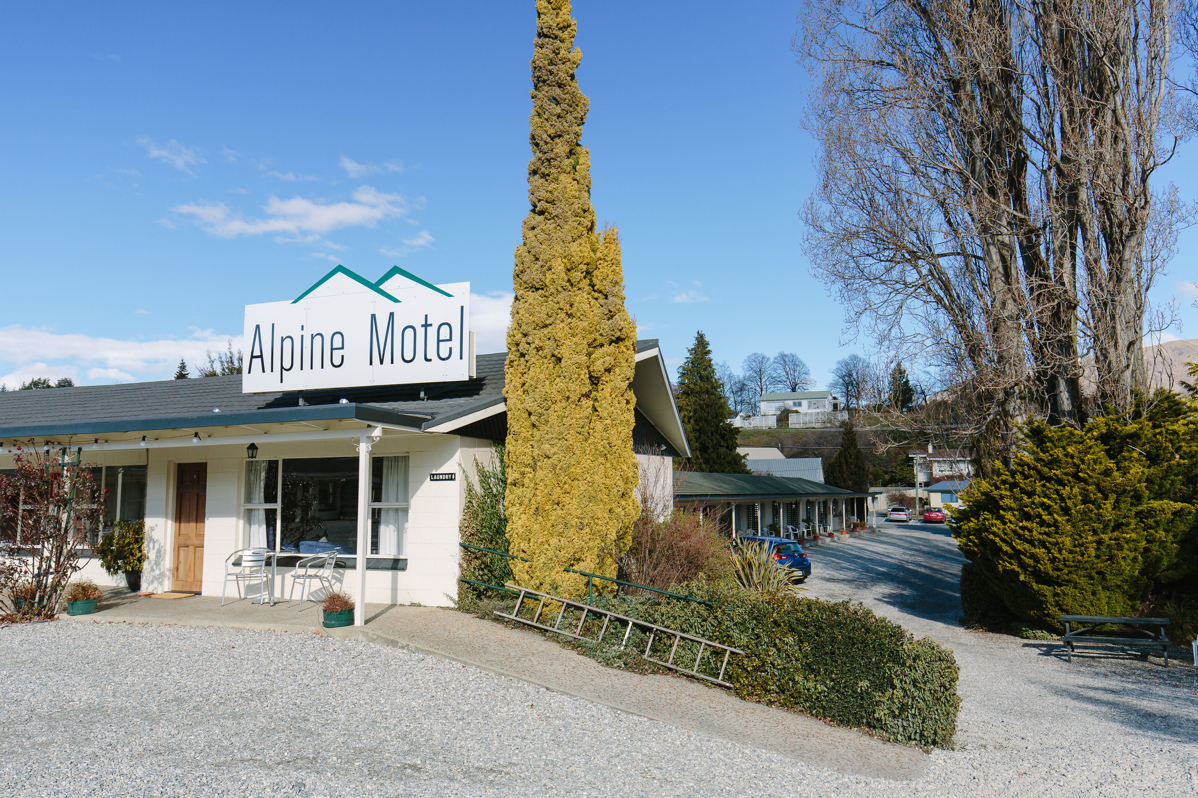 El Motel Alpine con un letrero llamativo, un porche cubierto y un camino de entrada de grava.